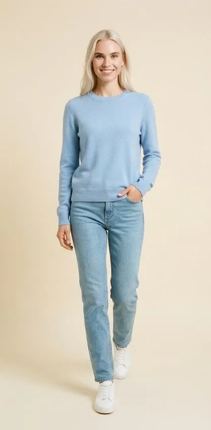 Modelo sonriente camina con jersey celeste, vaqueros claros y zapatillas blancas