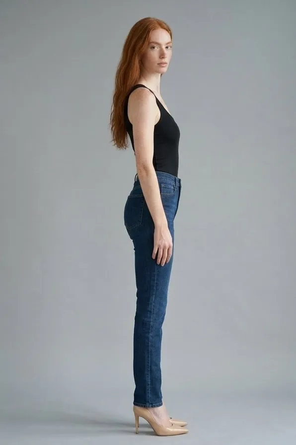 Modelo pelirroja de perfil con camiseta de tirantes negra y vaqueros oscuros