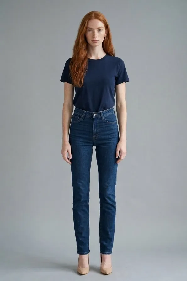Modelo pelirroja de frente con vaqueros azul oscuro de tiro alto, camiseta azul marino y tacones nude