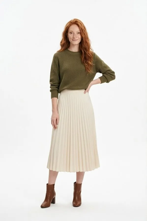 Modelo pelirroja con jersey verde oliva y falda plisada crema en una foto de catálogo